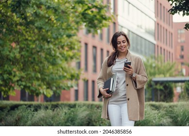 Beautiful Business Woman In Casual Outfit With A Laptop And Notebook Outdoor Speaks On Smartphone.