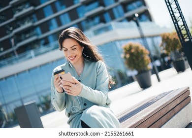 Beautiful Business Woman Enjoying Coffee Break On Free Time Outdoor With Favorite Music In Earphones, Millenial Female Listening Audio Book On Mobile App 