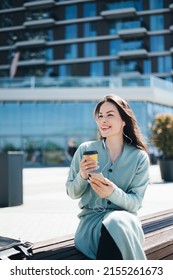 Beautiful Business Woman Enjoying Coffee Break On Free Time Outdoor With Favorite Music In Earphones, Millenial Female Listening Audio Book On Mobile App 