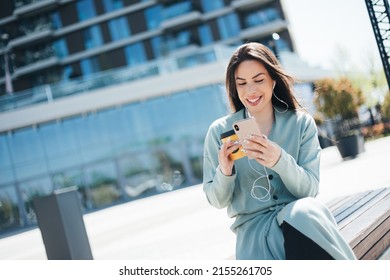 Beautiful Business Woman Enjoying Coffee Break On Free Time Outdoor With Favorite Music In Earphones, Millenial Female Listening Audio Book On Mobile App 