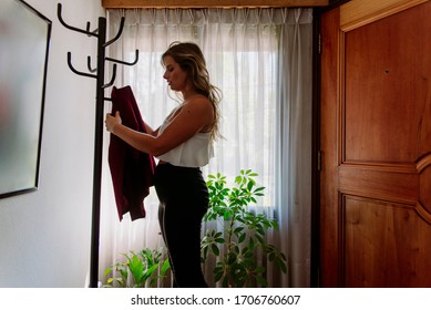 Beautiful Business Woman Hanging Her Red Jacket On The Office Coat Rack, With A Window In The Background, And Beautiful Plants, In Formal Wear.