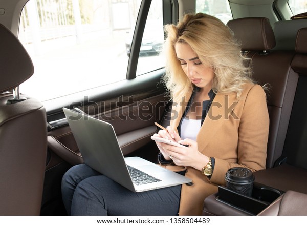 Beautiful business woman sitting in back seat of\
car and work on\
laptop.