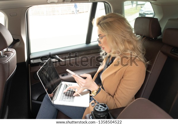 Beautiful business woman sitting in back seat of\
car and work on\
laptop.