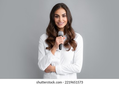 Beautiful Business Woman Is Speaking On Conference. Stylish Girl Singing Songs With Microphone, Holding Mic At Karaoke, Posing Against Gray Background.