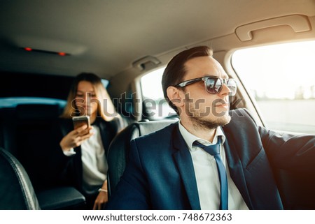 Beautiful business woman is using a smart phone and smiling while sitting on back seat in the car