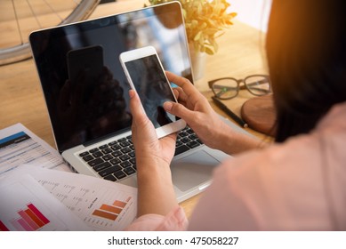 Beautiful Business Working Woman Using Iphone Ipad While Work With Laptop And Reading Report , Graphs , Charts, Document At Office. Business Woman Working At Her Desk.