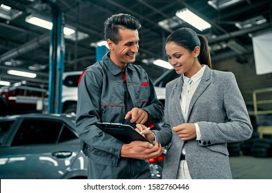 Beautiful businesswoman and auto service mechanic are discussing the work and signing documents. Car repair and maintenance. - Powered by Shutterstock