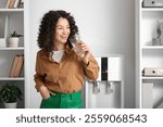 Beautiful businesswoman drinking water near cooler in office