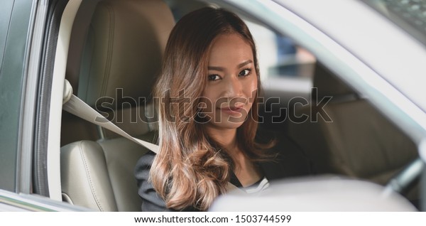 Beautiful businesswoman driving the car to the\
office while smiling to the camera\
