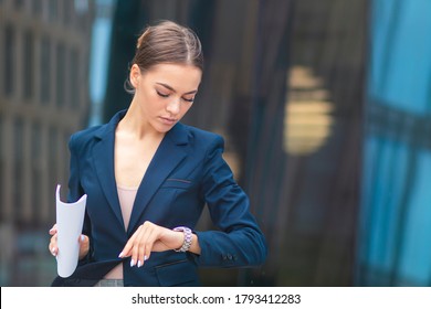 Beautiful businesswoman in formal suit, jacket, attractive woman in hurry, young girl , pretty lady with documents in hand looking at her wrist watch, checking time on watches, rushing, have no time