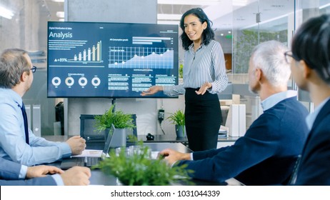 Beautiful Businesswoman Gives Report/ Presentation to Her Business Colleagues in the Conference Room, She Shows Graphics, Pie Charts and Company's Growth on the Wall TV. - Shutterstock ID 1031044339