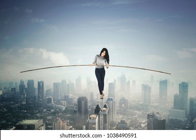 Beautiful businesswoman holding a stick to balance her body while walking on a rope. Shot above a city