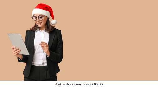 Beautiful businesswoman in Santa hat and with tablet computer on beige background with space for text - Powered by Shutterstock