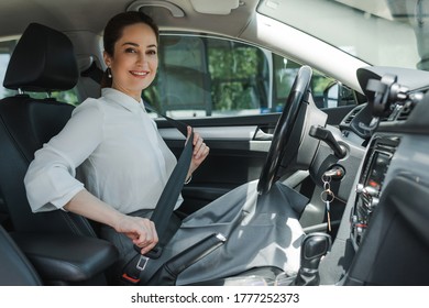 Beautiful businesswoman smiling at camera while holding seat belt in auto