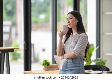 Beautiful businesswoman standing in the office while drinking her coffee - Shutterstock ID 2034142925