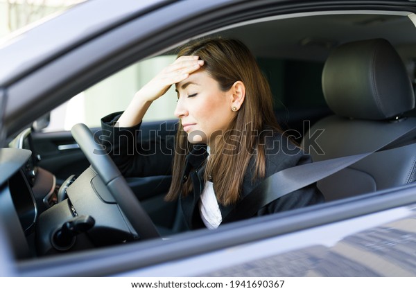 Beautiful businesswoman suffering from a\
headache and migraine because of stress work while driving her car\
and commuting to her office in the\
city