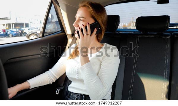 Beautiful\
businesswoman talking by smartphone and looking out of the car\
window while riding to work at\
morning.