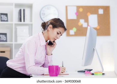 Beautiful Businesswoman Working At Her Desk In Office. Woman Talking On The Phone And Sitting In Front Of Computer Monitor,depth Of Field