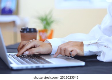 Beautiful businesswoman's hands typing on a laptop beside her office, wearing a white shirt, with a document next to it, a coffee cup. - Powered by Shutterstock