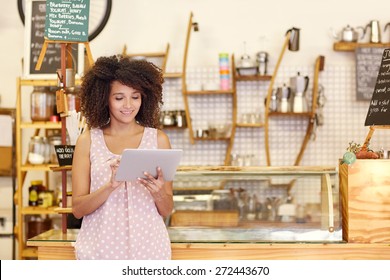 Beautiful Cafe Owner Running Her Small Business With The Help Of A Digital Tablet While Standing Near The Counter Of Her Coffee Shop