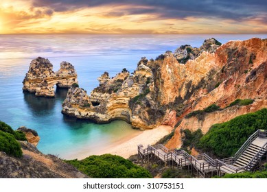 The beautiful Camilo Beach in Lagos, Portugal, with its magnificent cliffs and the blue ocean colorfully lit at sunrise