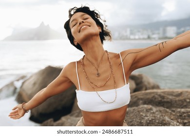 Beautiful carefree woman in a bohemian style, expressing peace and tranquility while meditating by the seaside. Perfect vacation scene at the beach with tan skin and ocean in the background. - Powered by Shutterstock