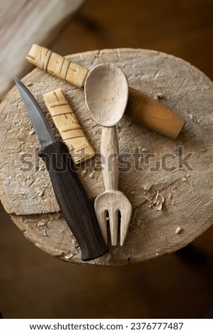 Beautiful carved wooden spoon and fork kitchen utensil with the carving knives on the top of a wood log in the workshop