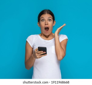 Beautiful Casual Woman Feeling Shocked While Reading Something On Her Phone Against Blue Background