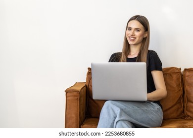 Beautiful casual woman with a laptop on a couch in a white isolated background - Shutterstock ID 2253680855