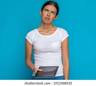 beautiful casual woman rolling eyes and feeling annoyed, holding her tablet against blue background