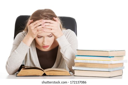 Beautiful casual woman student worried, scared is sitting by a desk and stack of books. Isolated on white.