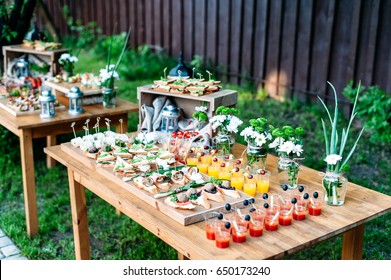 Beautiful catering banquet buffet table decorated in rustic style in the garden. Different snacks, sandwiches and cocktails. Outdoor.