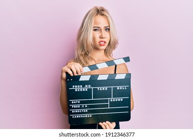 Beautiful Caucasian Blonde Girl Holding Video Film Clapboard Clueless And Confused Expression. Doubt Concept. 