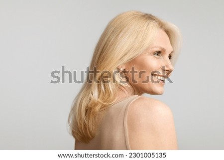 Beautiful caucasian blonde senior woman posing on grey background and smiling, aged lady enjoying beauty treatments result, free copy space