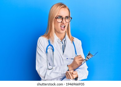 Beautiful caucasian blonde woman wearing doctor stethoscope holding clipboard angry and mad screaming frustrated and furious, shouting with anger. rage and aggressive concept. 