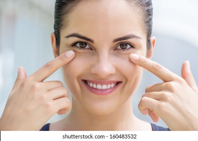 Beautiful Caucasian Brunette Young Woman Touching The Skin Under Her Eye.