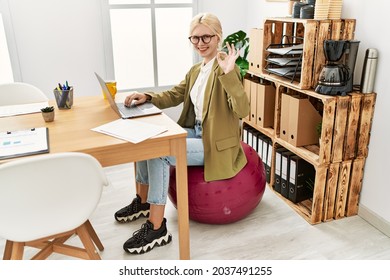 Beautiful caucasian business woman working at the office sitting on pilates ball doing ok sign with fingers, smiling friendly gesturing excellent symbol 