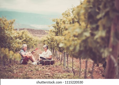 Beautiful Caucasian Couple Of Adult Senior 70 Years Old Enjoy The Time In The Summer Playing An Ukulele Together In The Vineyard. Outdoor Countryside Happy People Concept