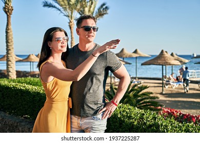 Beautiful Caucasian Couple On Sea Vacation In A Tropical Resort. Woman Is Pointing At Something Interesting On The Horizon.