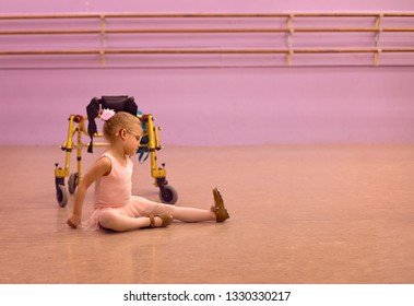 Beautiful Caucasian Female Child Tap Dancer Wearing Pink Ballet Leotard Dances Beside Her Gold Walker Mobility Aid While Wearing Glasses And Hearing Aids 