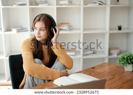 A beautiful caucasian female student is studying remotely. She is sitting at a table at home with a laptop and a notepad and concentrated is watching a video conference, Thinking.