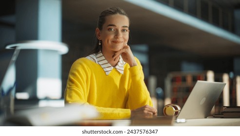 Beautiful Caucasian Female Student Working on Her School Thesis on a Laptop Computer in a Modern Library. Young Smart Woman Looking at Camera, Smiling. Girl Wearing a Vivid Yellow Sweater - Powered by Shutterstock