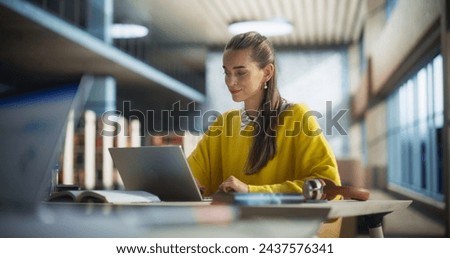 Beautiful Caucasian Female Student Working on Her College Degree Thesis on a Laptop Computer in Library. Young Stylish Female in a Yellow Jumper Studying an Online Course Alone in a Reading Hall