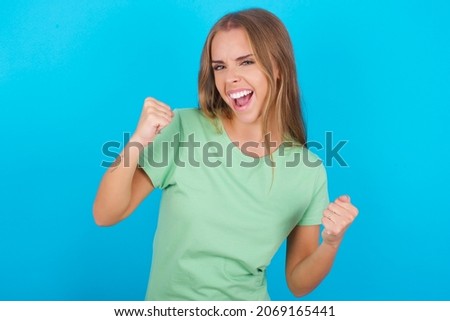Beautiful caucasian girl wearing green T-shirt over isolated background celebrating surprised and amazed for success with arms raised and eyes closed. Winner concept.