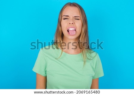 Beautiful caucasian girl wearing green T-shirt over isolated background sticking tongue out happy with funny expression. Emotion concept.