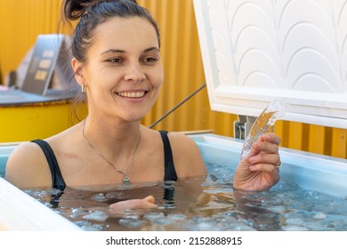 Beautiful Caucasian girl or woman smiling and bathing in the cold water among ice cubes holding a piece of ice in her hand. Wim Hof Method, cold therapy, breathing techniques, yoga and meditation