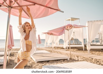 Beautiful caucasian lady stretches arms upstairs looking to side on deserted beach. Blonde with bandage on her head in separate swimsuit and shirt on top. Rest and recovery concept. - Powered by Shutterstock