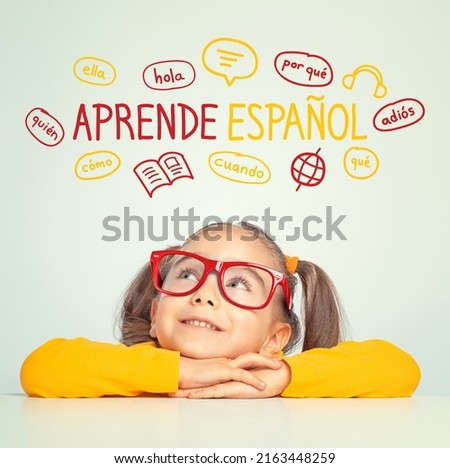 Beautiful caucasian little girl with eyeglasses looking at  Learn Spanish text in Spanish and illustrations. English: Learn English. Foreign language learning concept.
