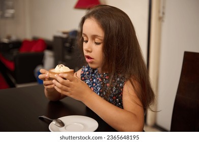 Beautiful Caucasian little girl in stylish casual dress, eating a delicious lemon cake at home. Sweet food concept. French patisserie and boulangerie concept