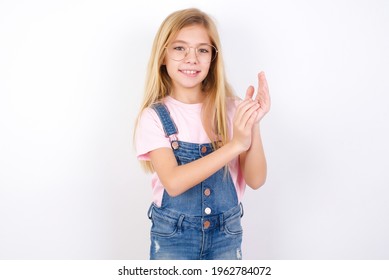 beautiful caucasian little girl wearing jeans overall over white background clapping and applauding happy and joyful, smiling proud hands together.